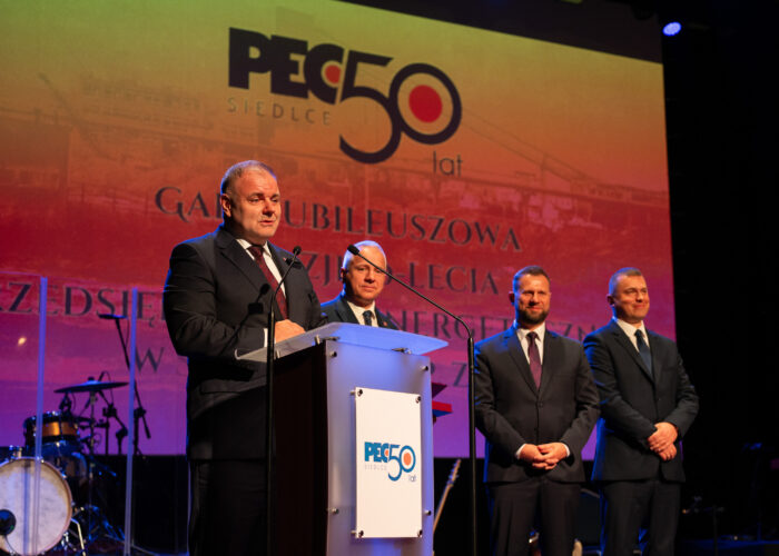 Przemowa Przewodniczącego Rady Miasta Siedlce Roberta Chojeckiego podczas gali jubileuszowej, w tle Prezydent Miasta Siedlce oraz Zarząd Przedsiębiorstwa Energetycznego w Siedlcach Sp. z o.o.