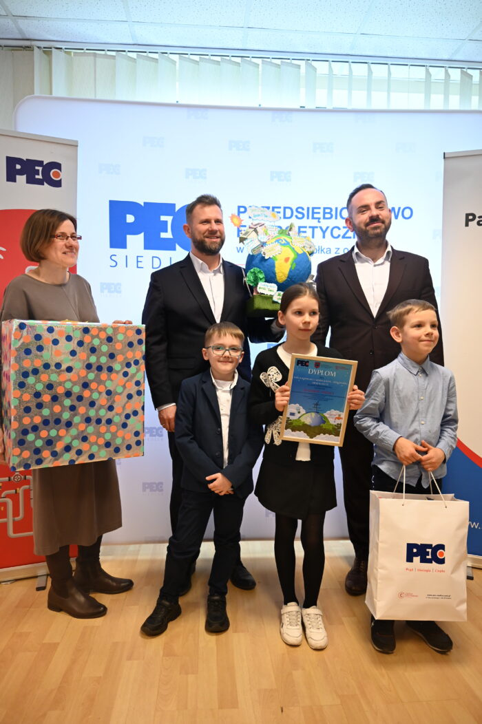 Naczelnik Gabinetu Prezydenta Miasta Siedlce Piotr Woźniak, Prezes Zarządu PEC Siedlce Wojciech Pawlik oraz laureatka projektu wraz z uczniami. Widoczna praca konkursowa.